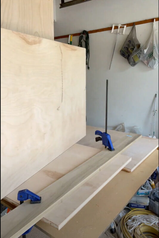 A scrap piece of wood attached to cabinet piece with clamps.