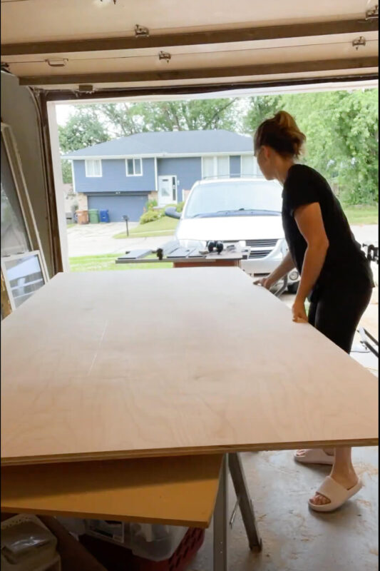 Woman moving heavy sheet of plywood to build refrigerator cabinet.