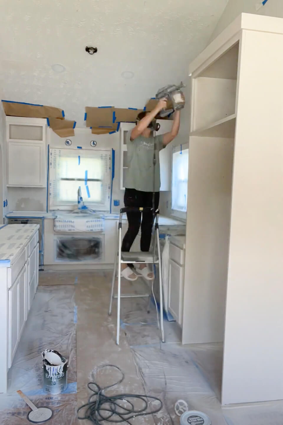 Woman using paint sprayer to paint her kitchen cabinets.