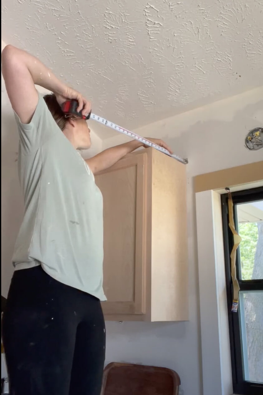 Woman measuring for extending kitchen cabinets to the ceiling.
