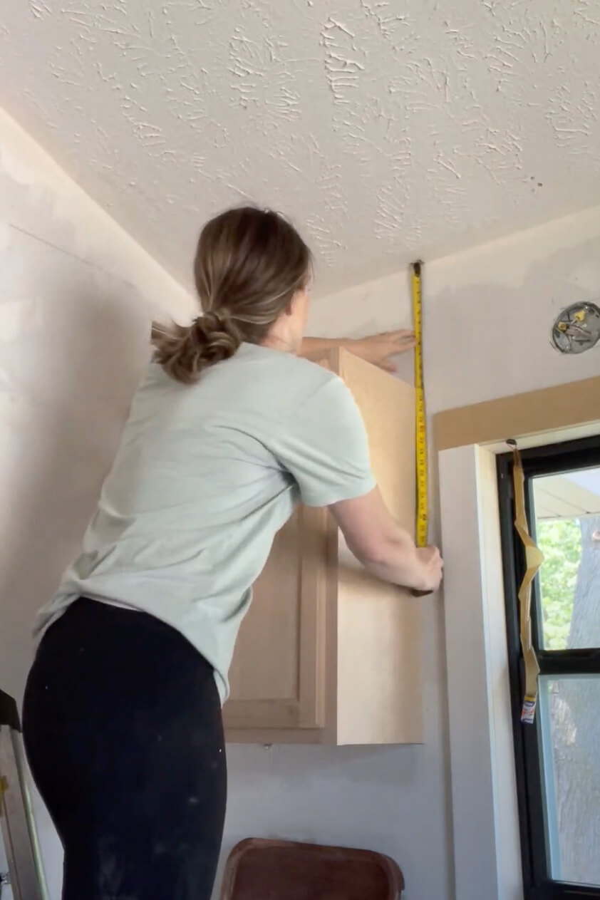 Woman measuring for extending kitchen cabinets to the ceiling.