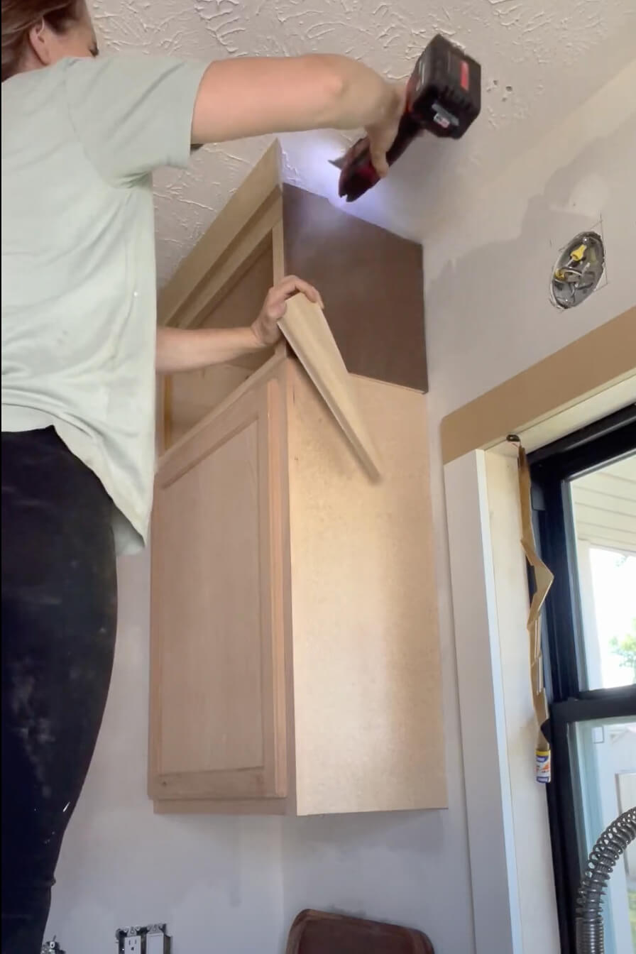 Woman adding crown molding to her kitchen cabinets.