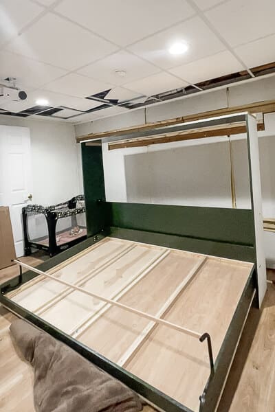 Partially installed horizontal Murphy bed frame attached to green wall cabinet unit