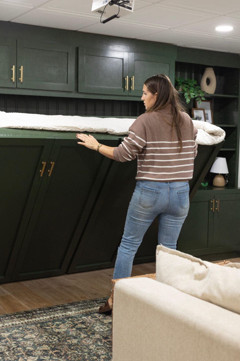 Woman folding down custom-built horizontal Murphy bed with green cabinet fronts in a finished basement guest room