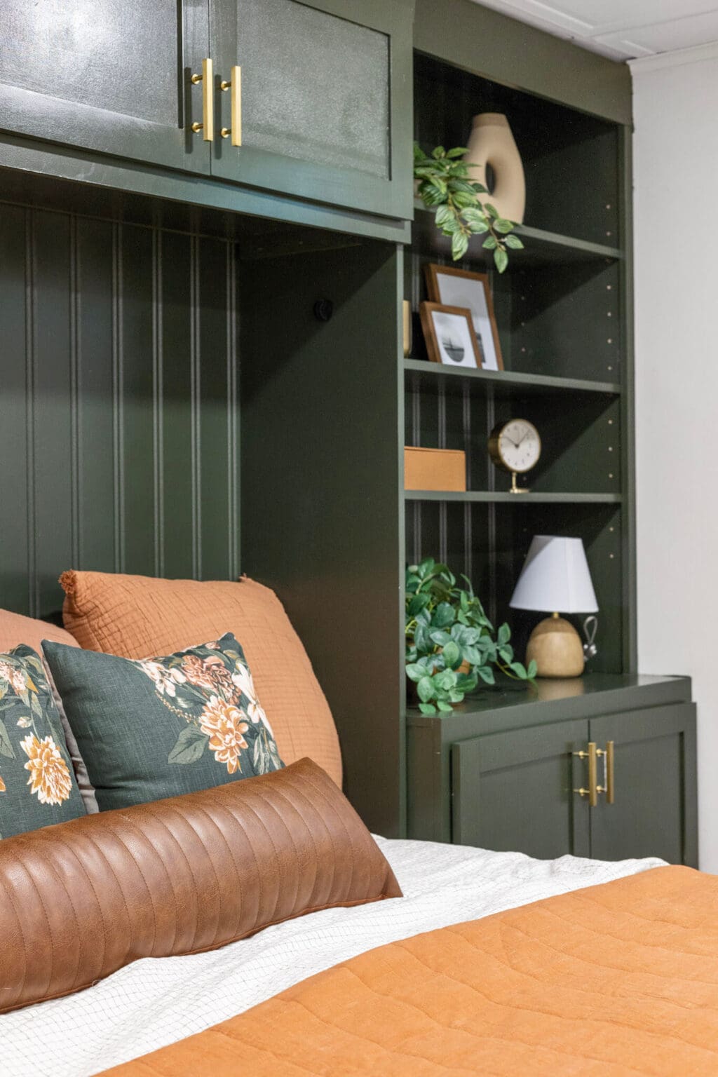 Close-up of built-in shelving beside horizontal Murphy bed styled with greenery, decor, and a small lamp
