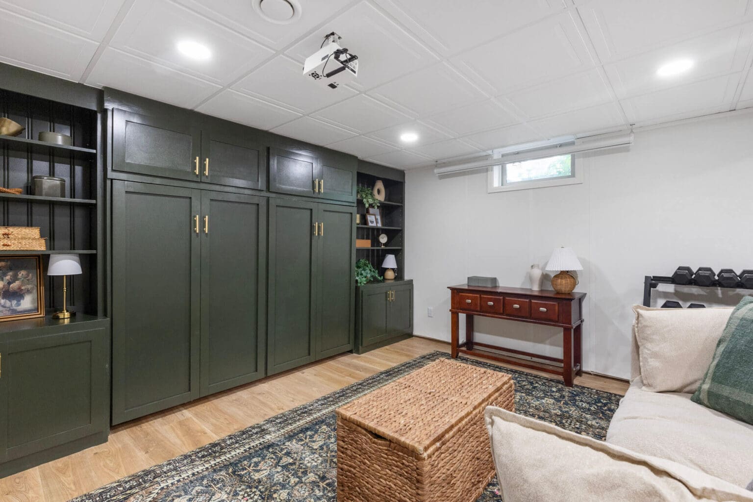 Wall of built-in cabinetry with horizontal Murphy bed closed and fully concealed, blending into green cabinets with brass hardware