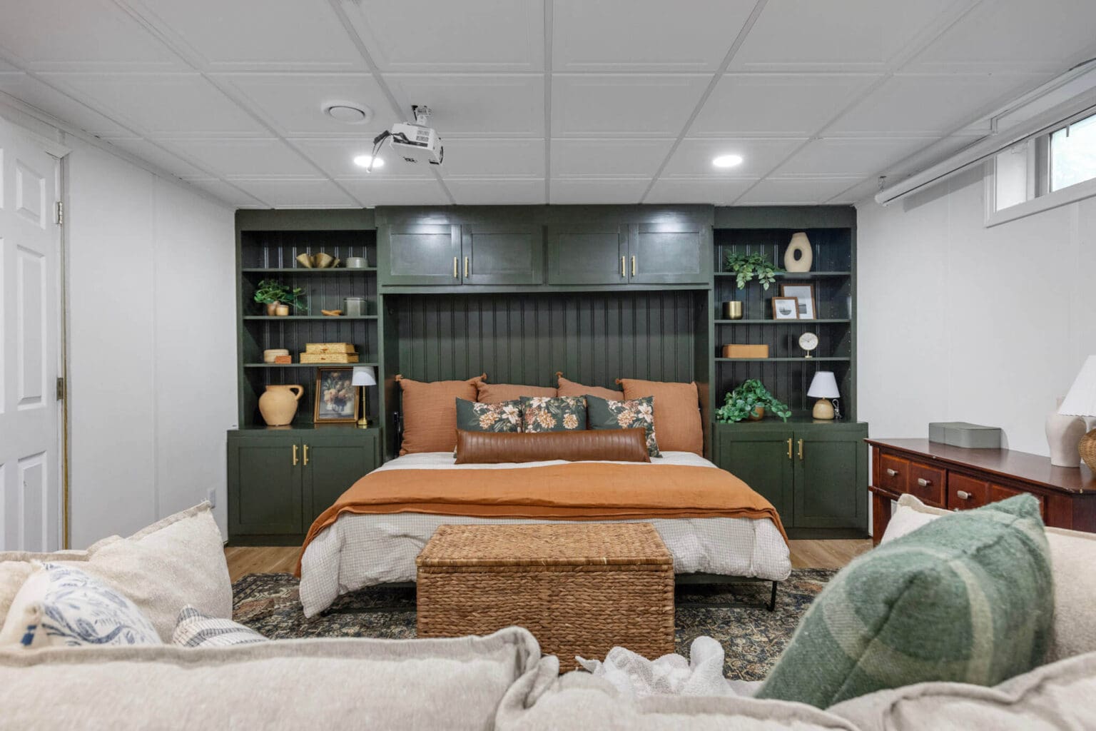 Horizontal Murphy bed in the open position with orange and floral bedding, styled with built-in cabinets and a wicker trunk at the foot