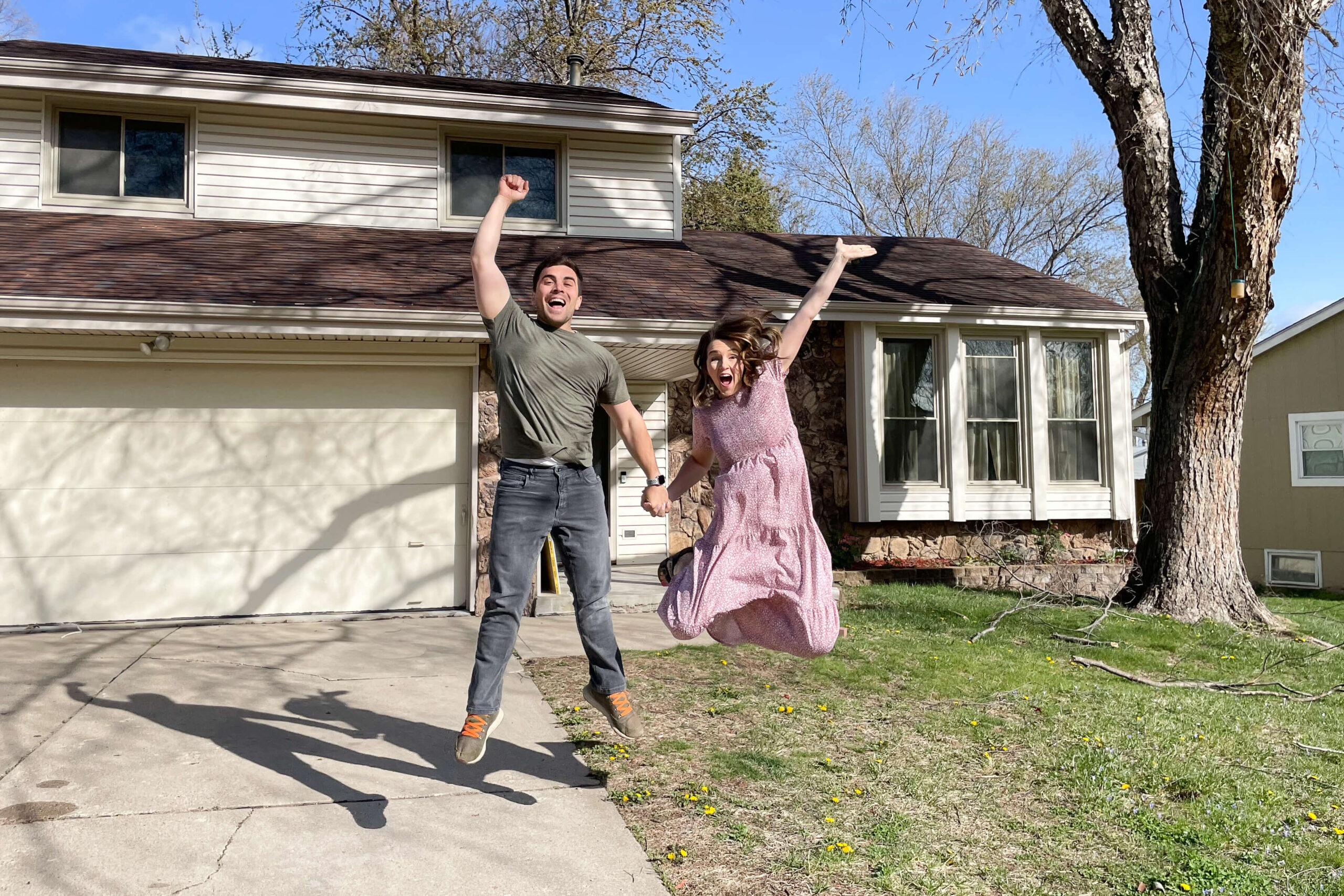 New homeowners jumping up excited in front of the fixer upper they purchased.