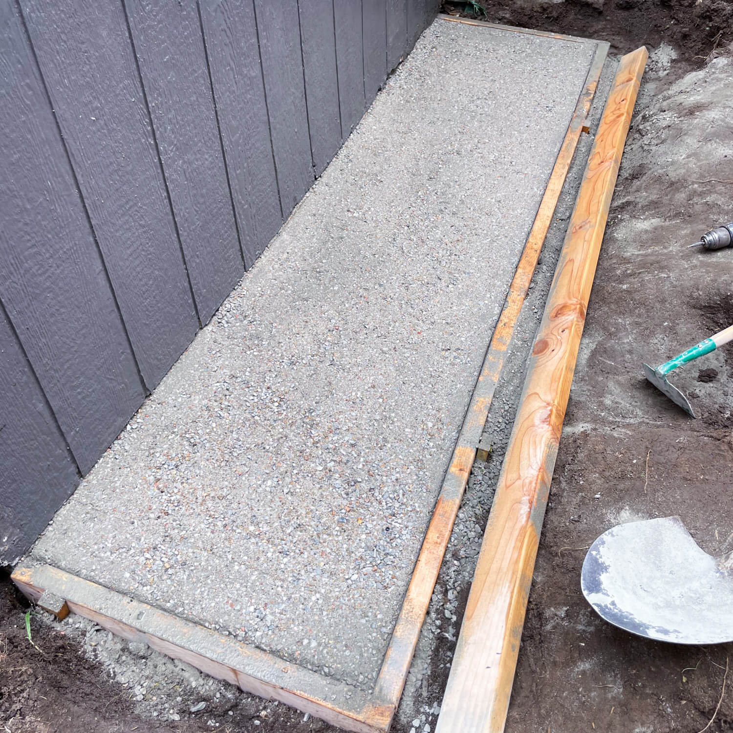 A small dry pour concrete pad behind a backyard shed.