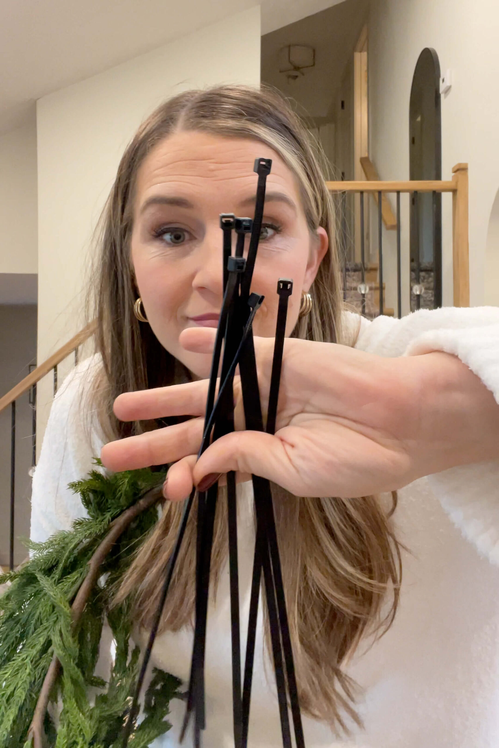 Using zip ties to attach Christmas garland on a staircase.