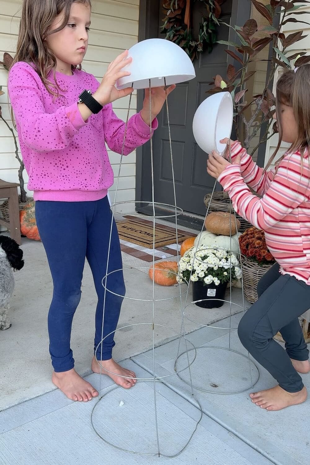 Kids building tall sheet ghost frames with tomato cages and foam domes by the front door.