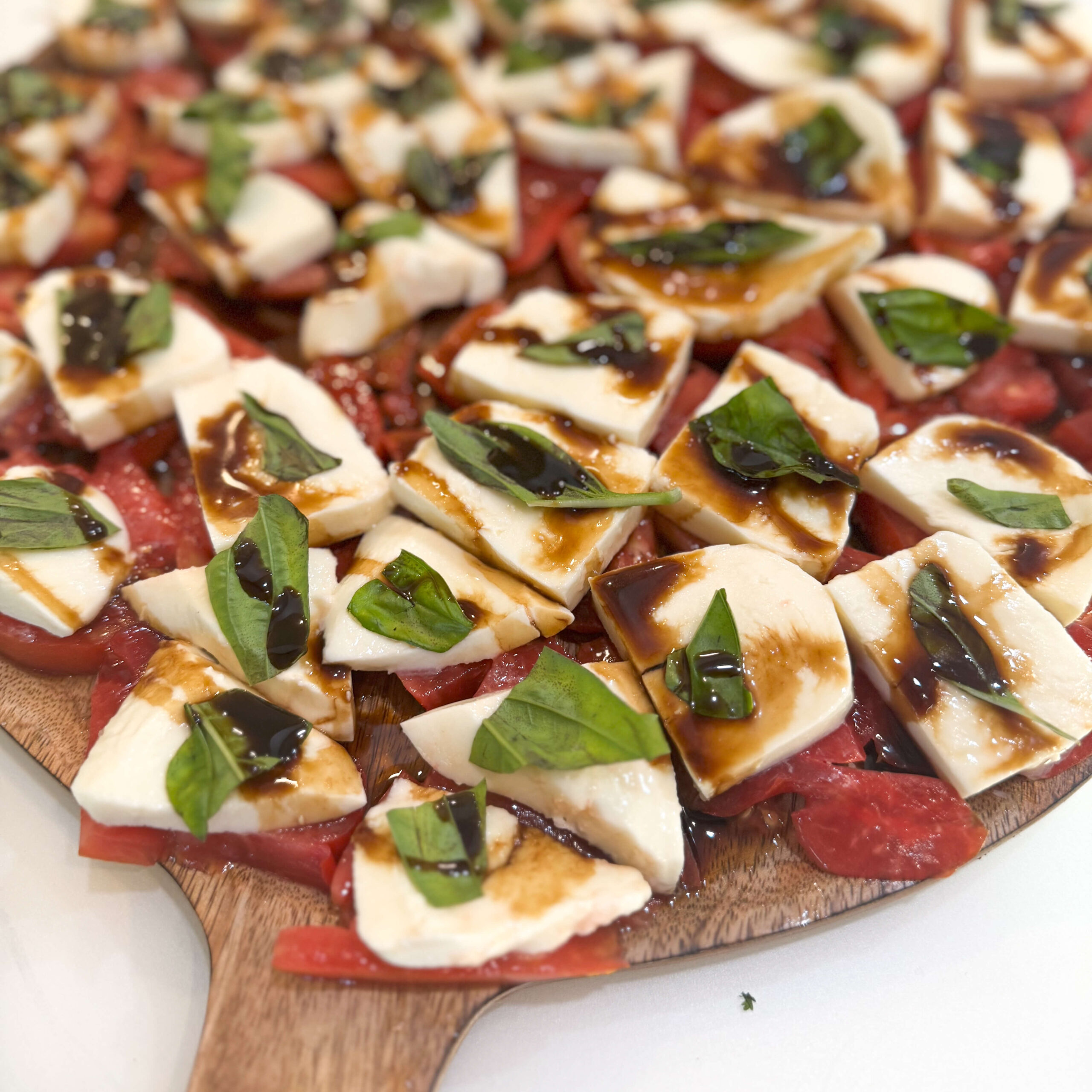 A fresh Caprese salad arranged on a wooden board, featuring layers of sliced tomatoes, mozzarella cheese, fresh basil leaves, and a generous drizzle of balsamic glaze—perfect for a caprese salad recipe.