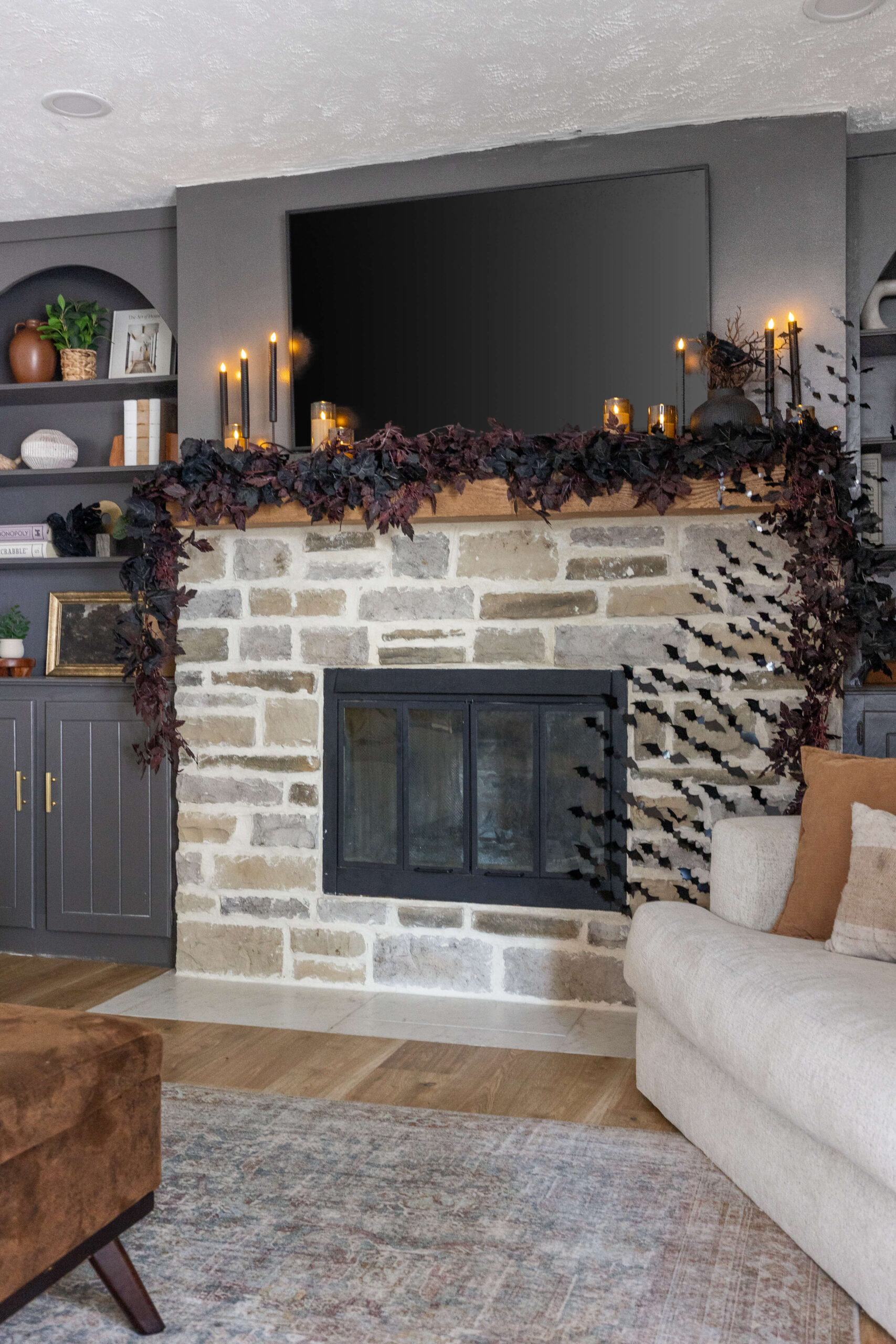 Living room and fireplace decorated for Halloween with dark garlands, spooky candles, and bats.