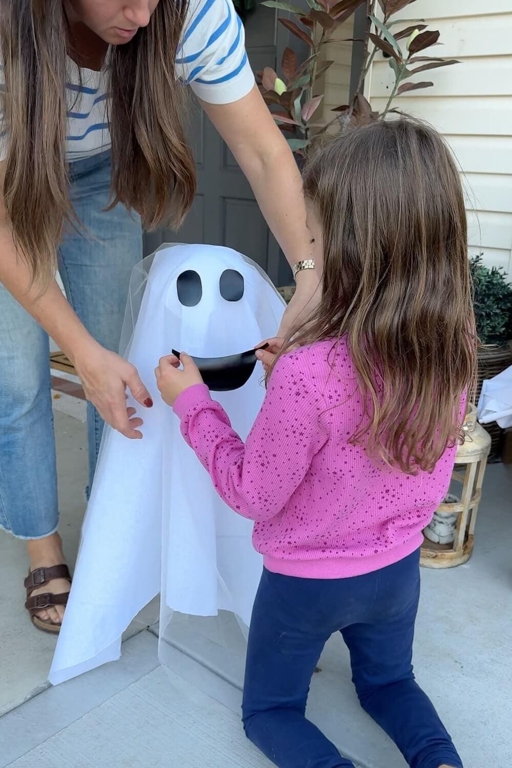 Child helping place a vinyl smile on a small sheet ghost during the DIY porch ghost project.