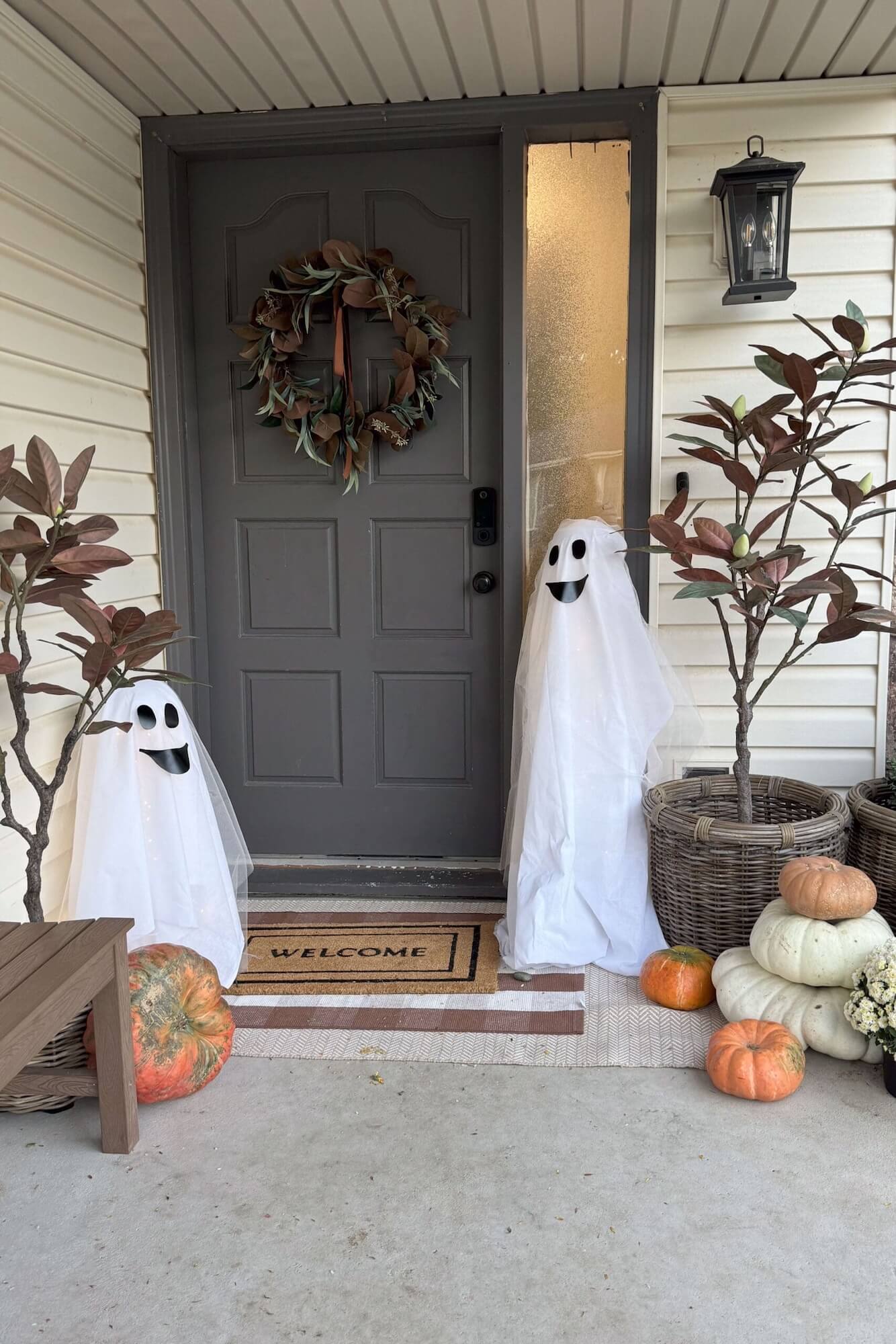Two porch ghost decorations flanking the gray front door with pumpkins and wicker planters.