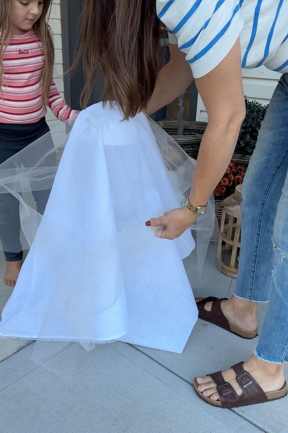 Draping white fabric and tulle over a ghost frame while a child helps on the porch.