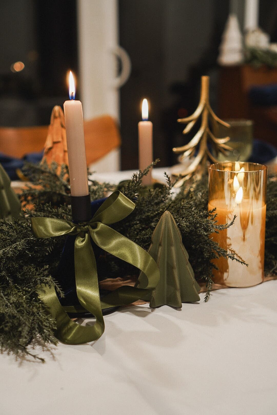 Close-up of candles tied with green satin ribbon and mini Christmas trees on a beautifully arranged Christmas tablescape.