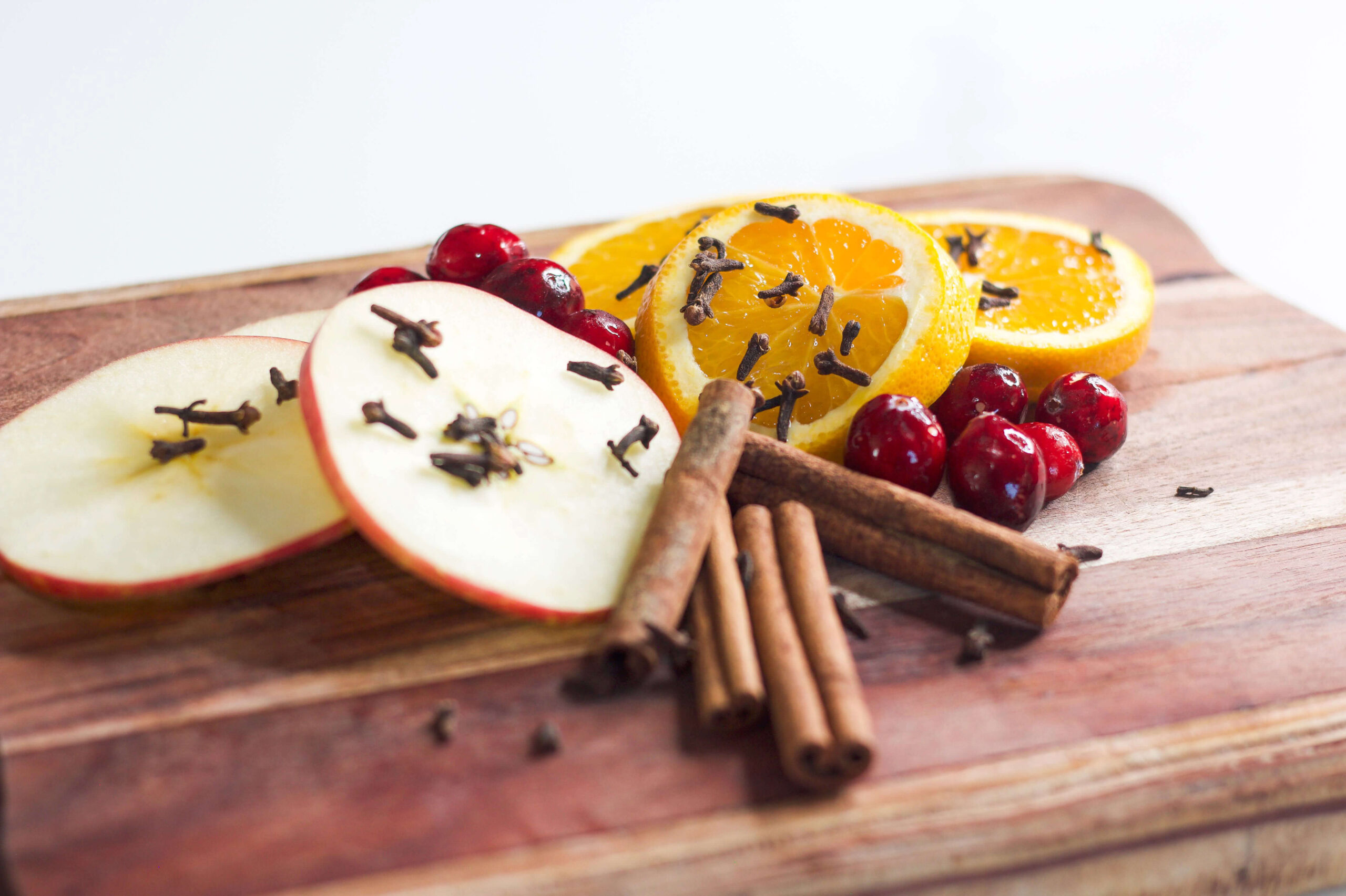 Sliced apples and oranges with cloves, cranberries, and cinnamon sticks on a wooden cutting board for a Christmas simmer pot."