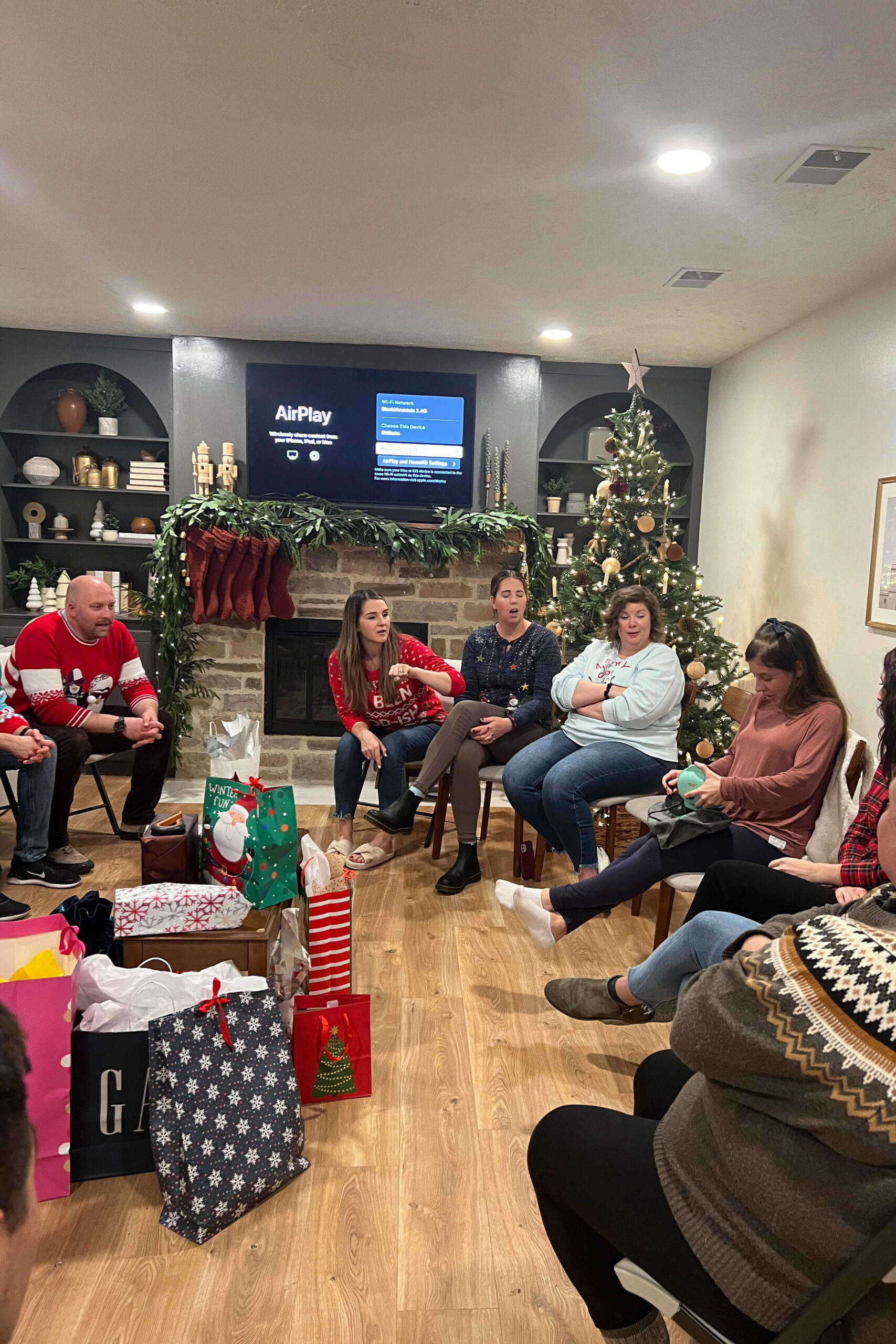 Friends playing White Elephant during a holiday party, surrounded by Christmas decorations and gifts, as part of christmas party games.