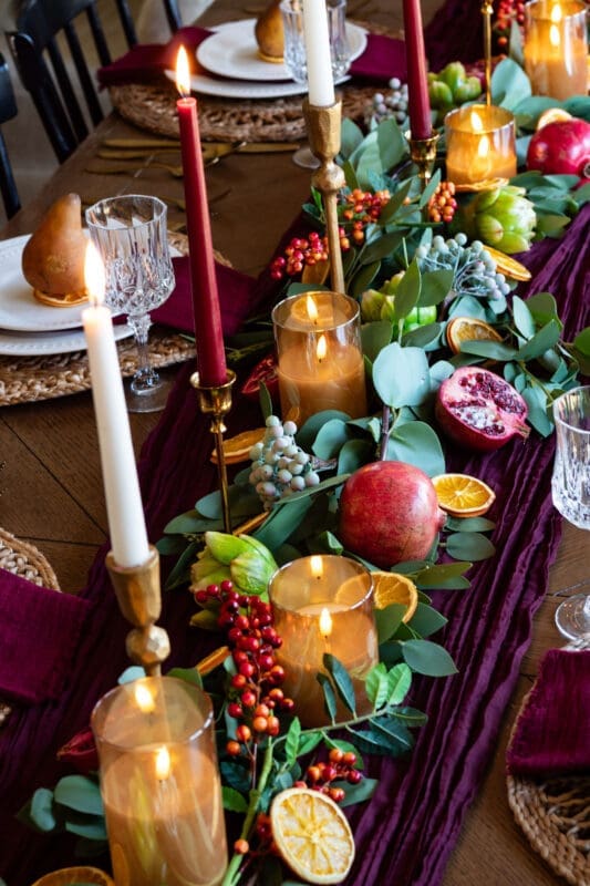 Thanksgiving tablescape centerpiece with burgundy and ivory taper candles, pomegranates, eucalyptus, and brass candlesticks