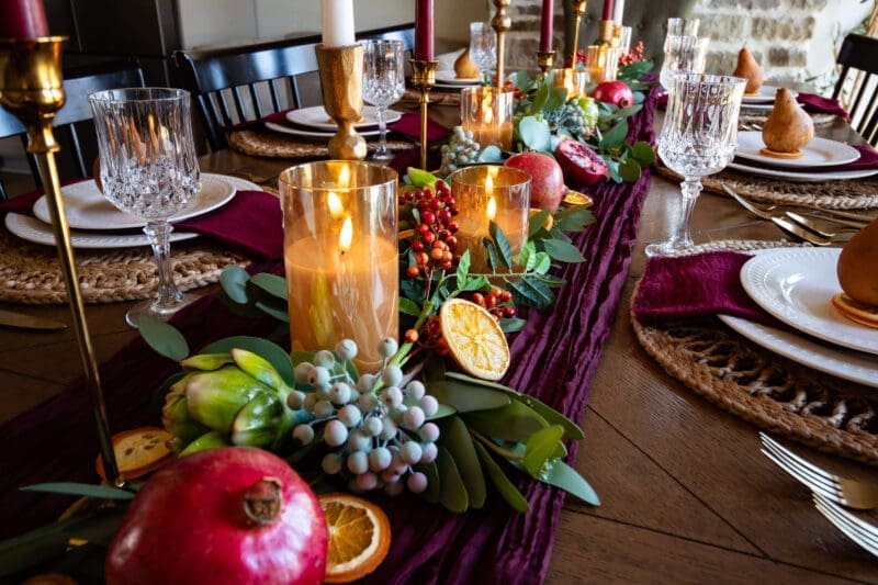 Burgundy Thanksgiving decor with pomegranates, gold candlesticks, and glass goblets along the table
