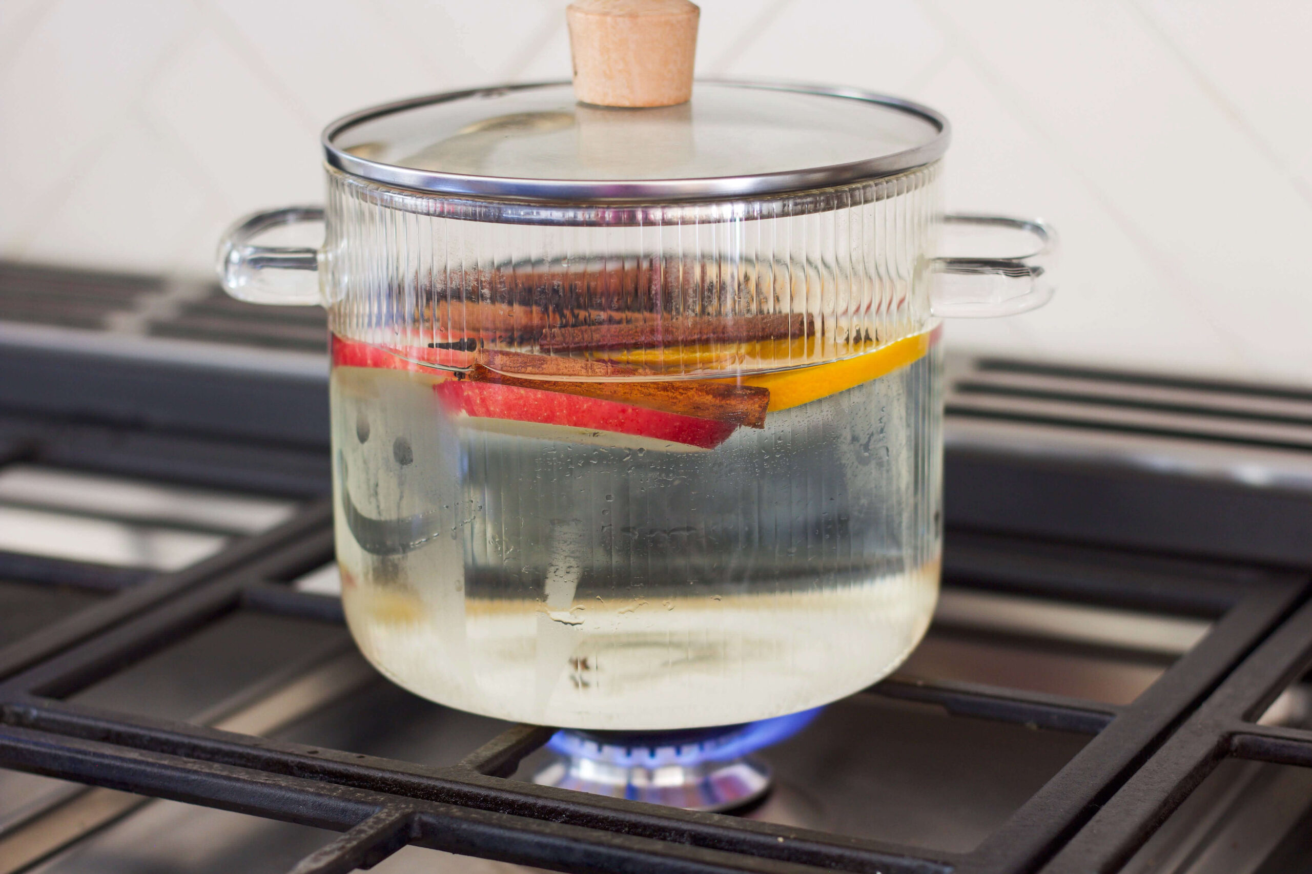 Close-up of a Christmas simmer pot with cinnamon sticks, apples, and oranges simmering on the stove.