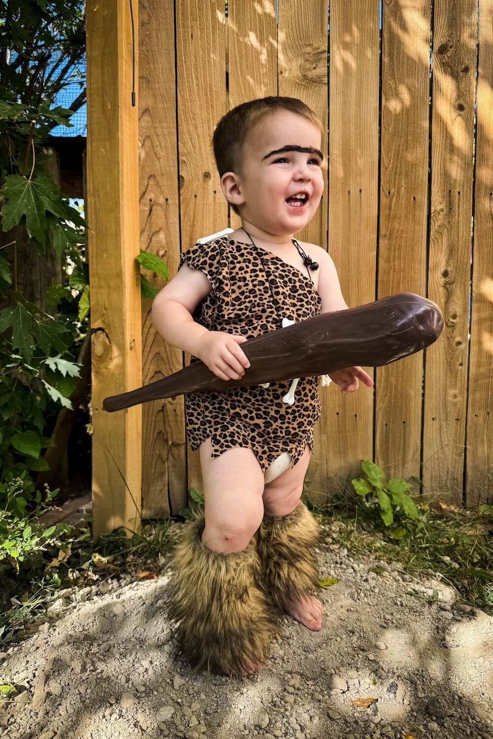 Toddler in leopard-print DIY caveman outfit with faux-fur boots holding a toy club.