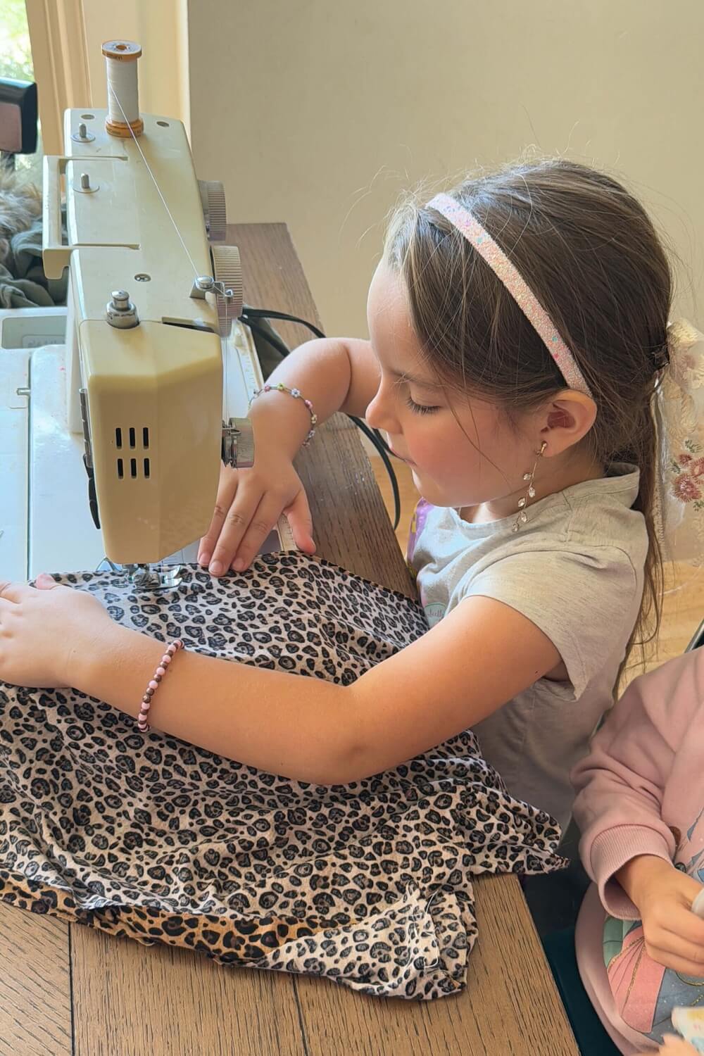 Girl sewing leopard-print fabric on a home sewing machine for a costume.