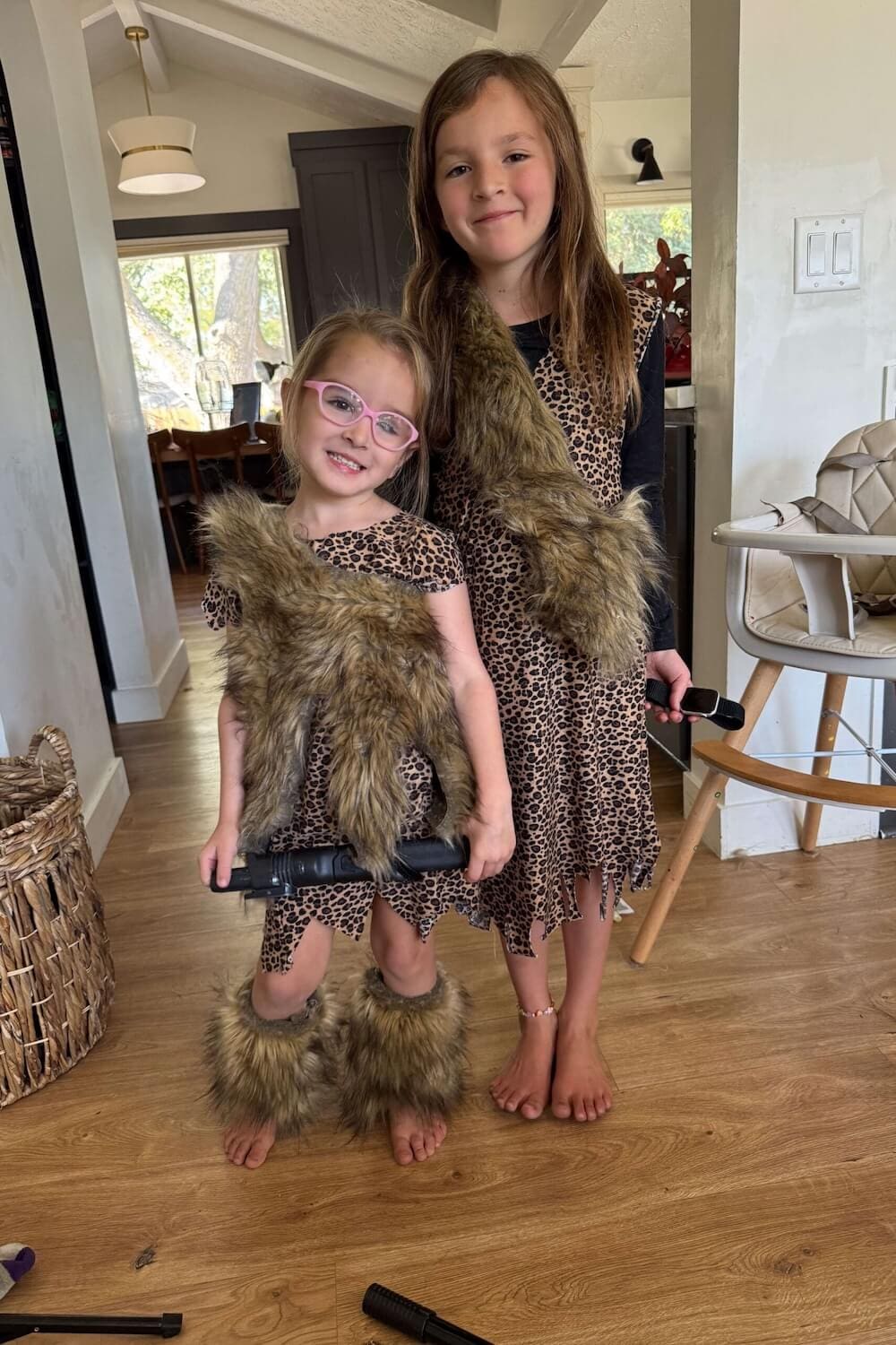 Two kids in leopard-print caveman outfits with faux-fur sashes, smiling indoors.