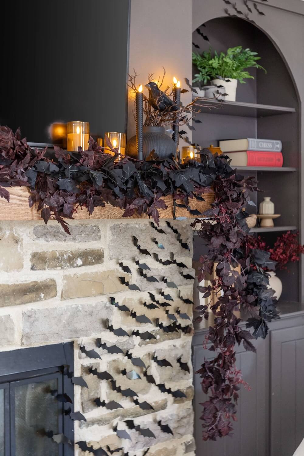 Halloween mantel decor with candles, dark foliage, and paper bats
