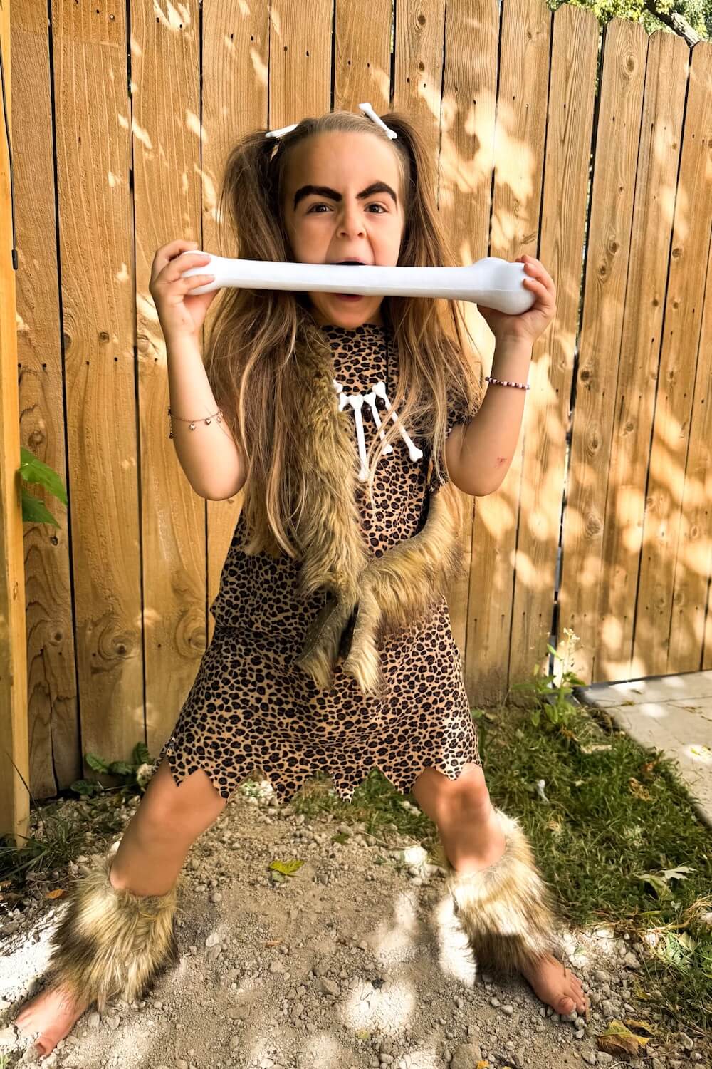 Kid in caveman costume pretending to bite a jumbo bone prop