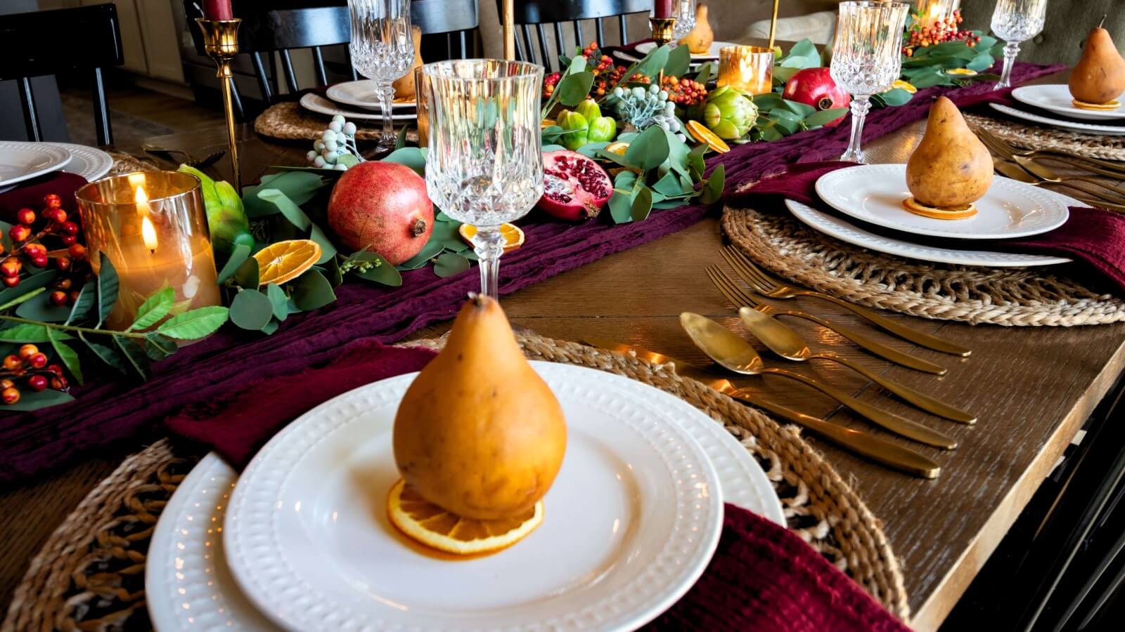 Burgundy Thanksgiving tablescape with eucalyptus garland, pomegranates, gold candlesticks, and glass goblets