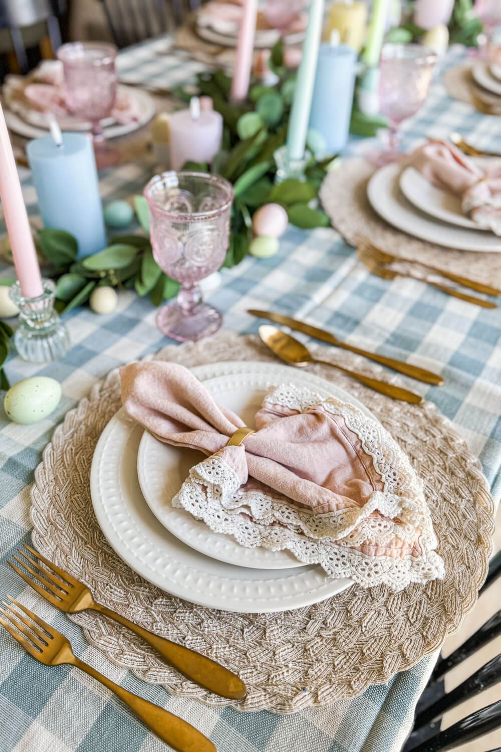 Blue gingham tablecloth with pastel candles, eucalyptus garland, and speckled eggs for a fresh Easter table decor look
