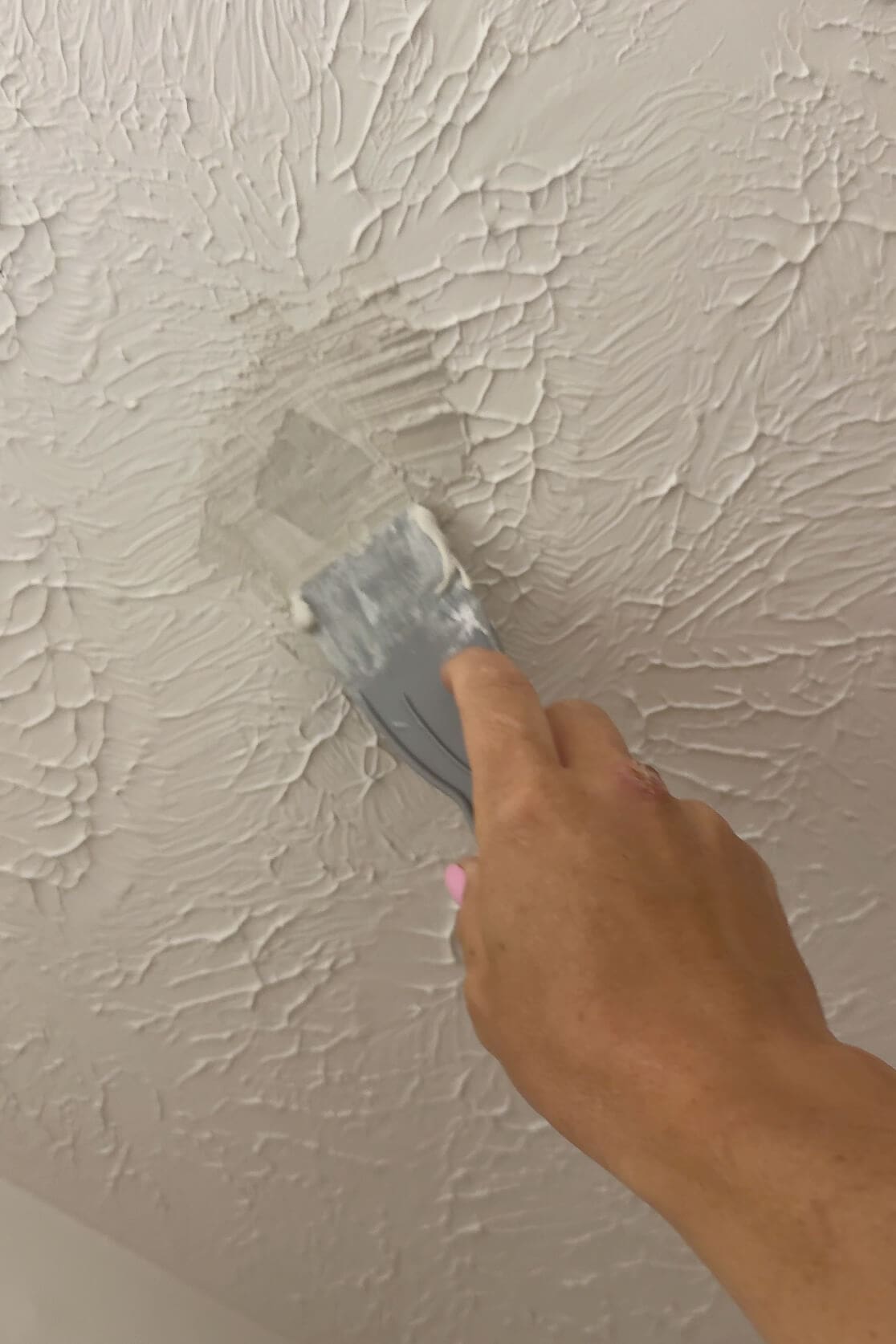 Hand using a putty knife to apply joint compound on a textured ceiling