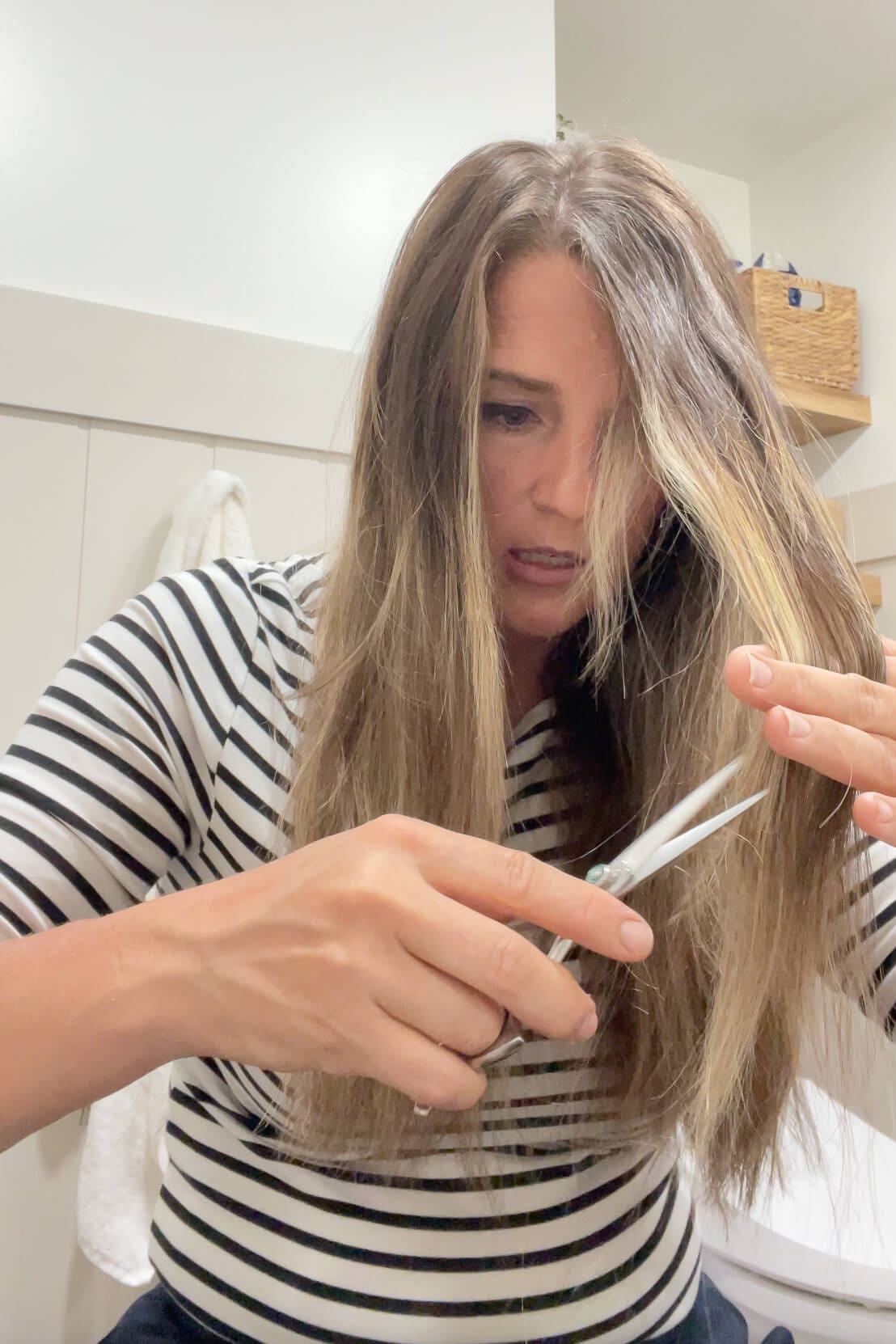 Trimming the ends of long hair to blend layers evenly during a home haircut.

