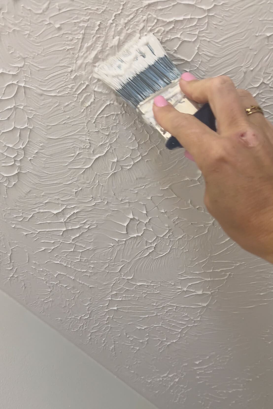 Hand using a brush to paint over patched texture on a white ceiling