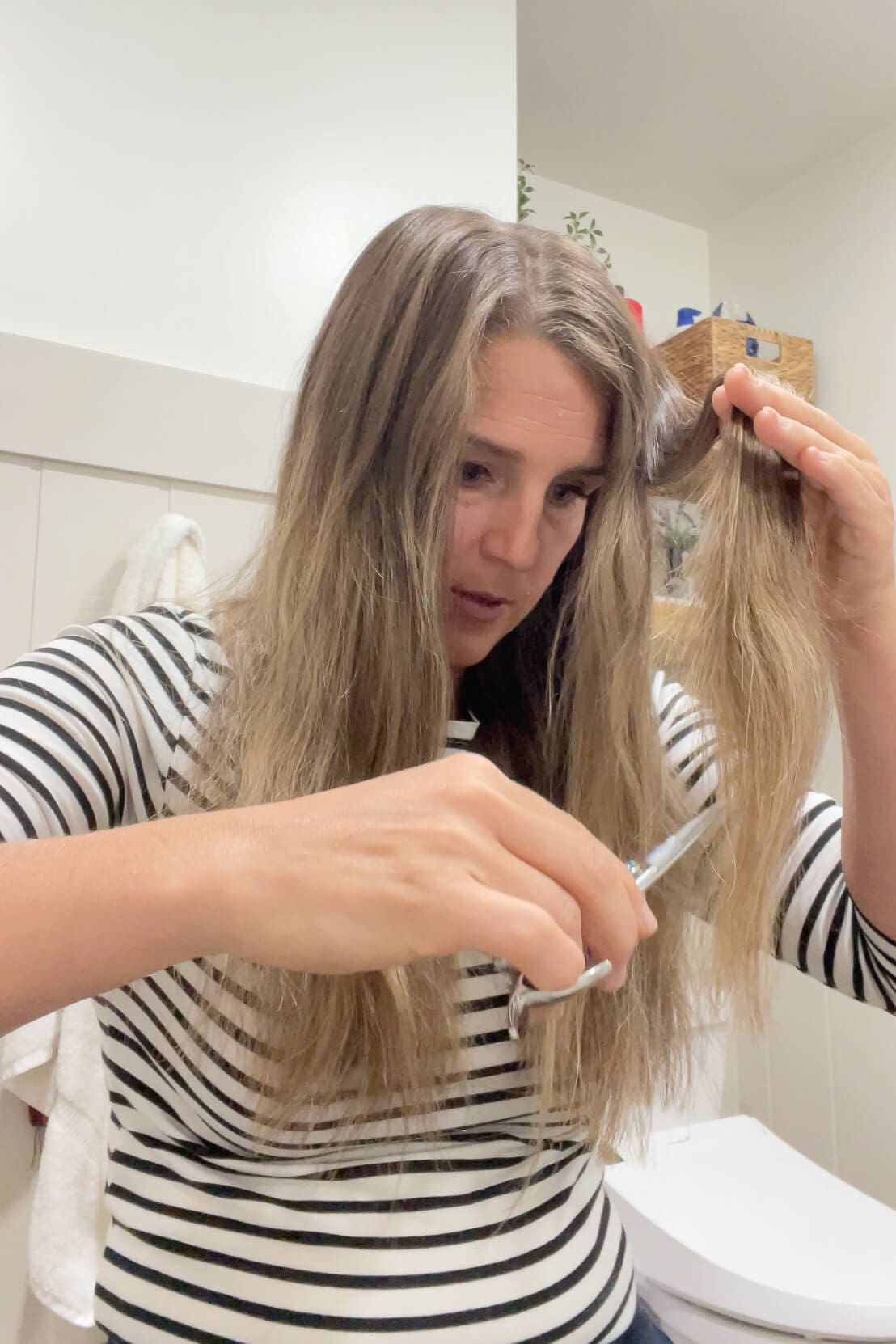 Focused DIY haircut in progress, trimming a mid-length section for blended layers.