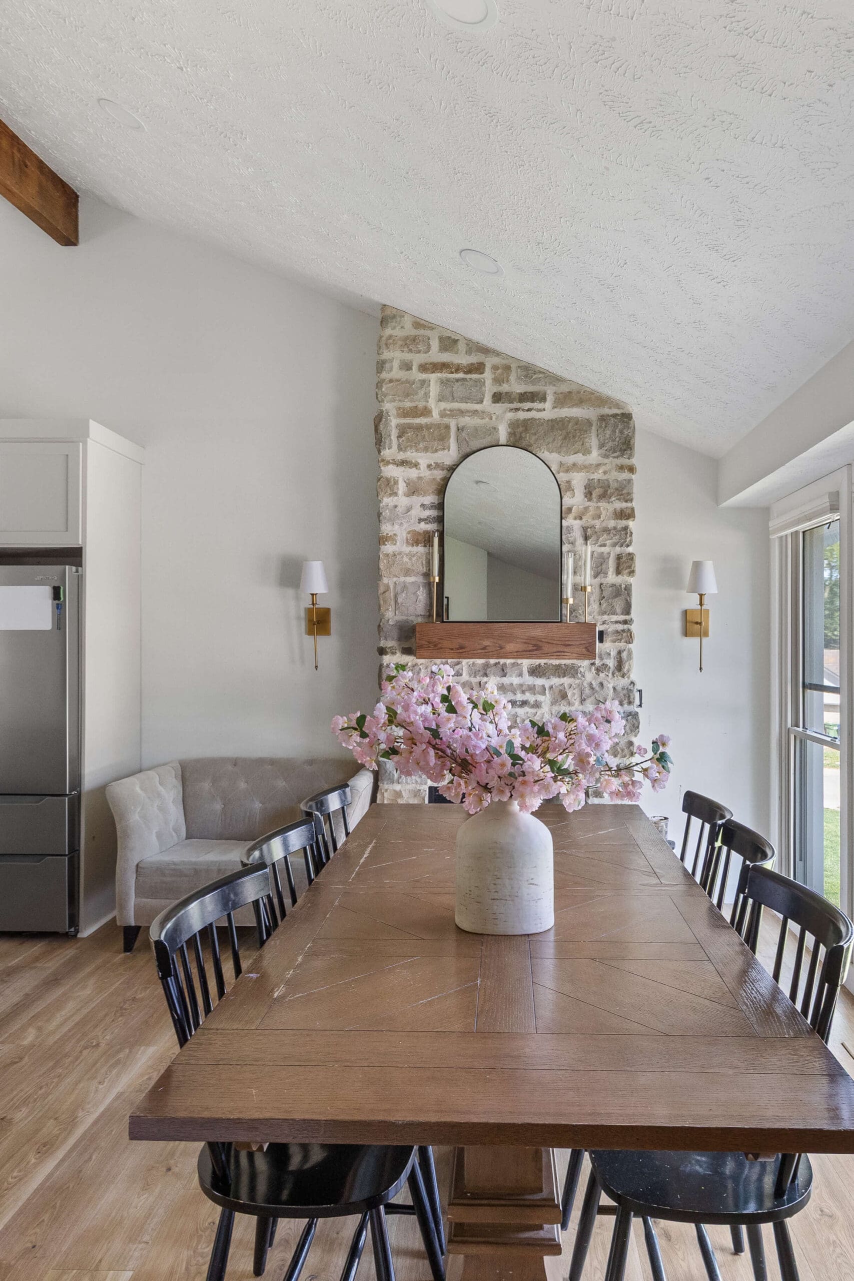 Bright dining room with wood table, white textured ceiling, and natural stone fireplace