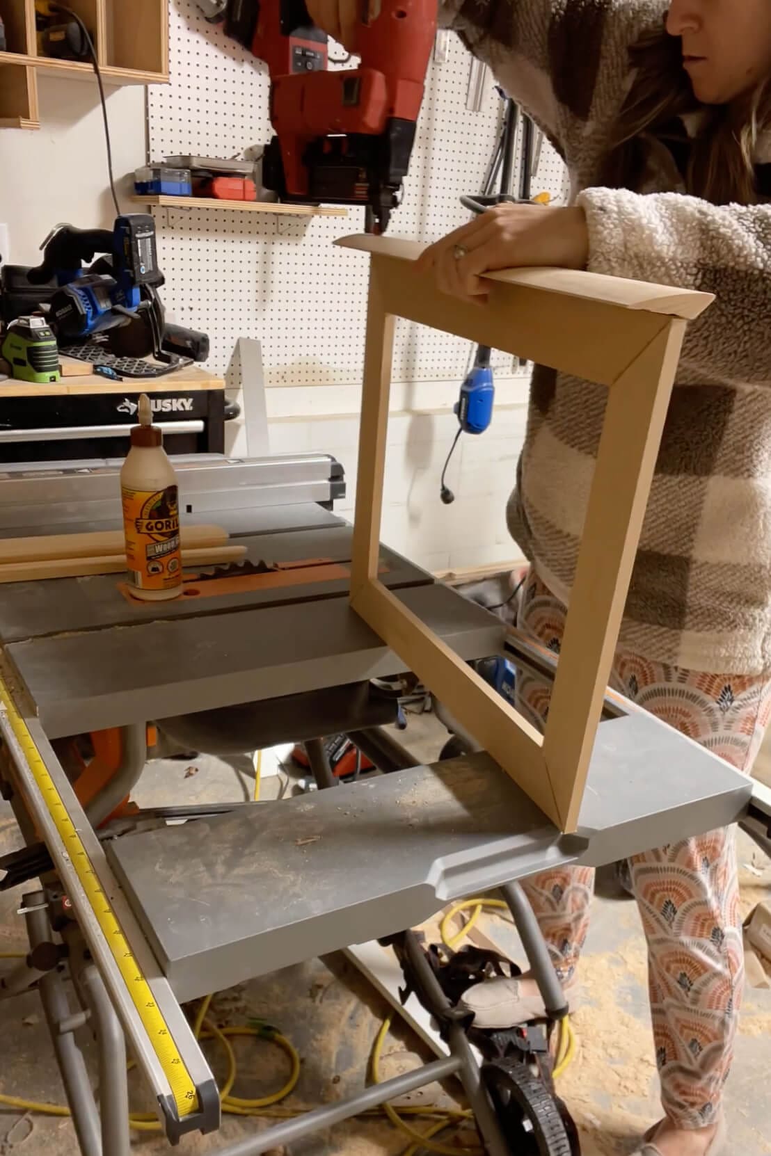 Using a nail gun to secure the corners of a handmade wooden frame in a DIY project.