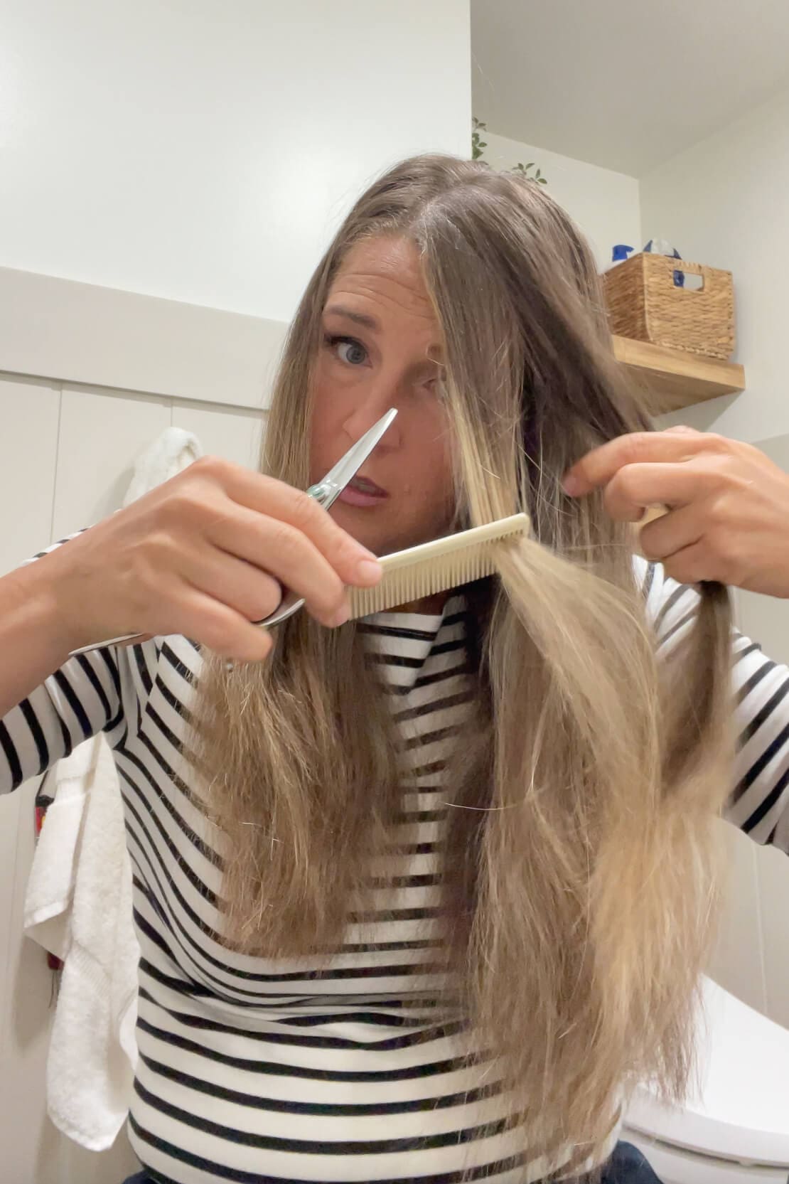 Using a comb and scissors to trim face-framing layers in long straight hair at home.