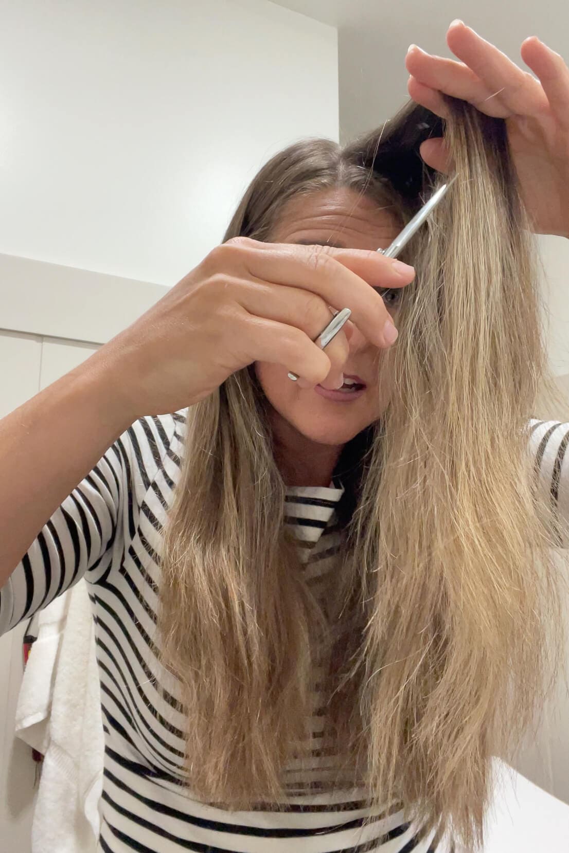 Trimming a section of hair using point-cutting technique to soften layers during a DIY haircut.
