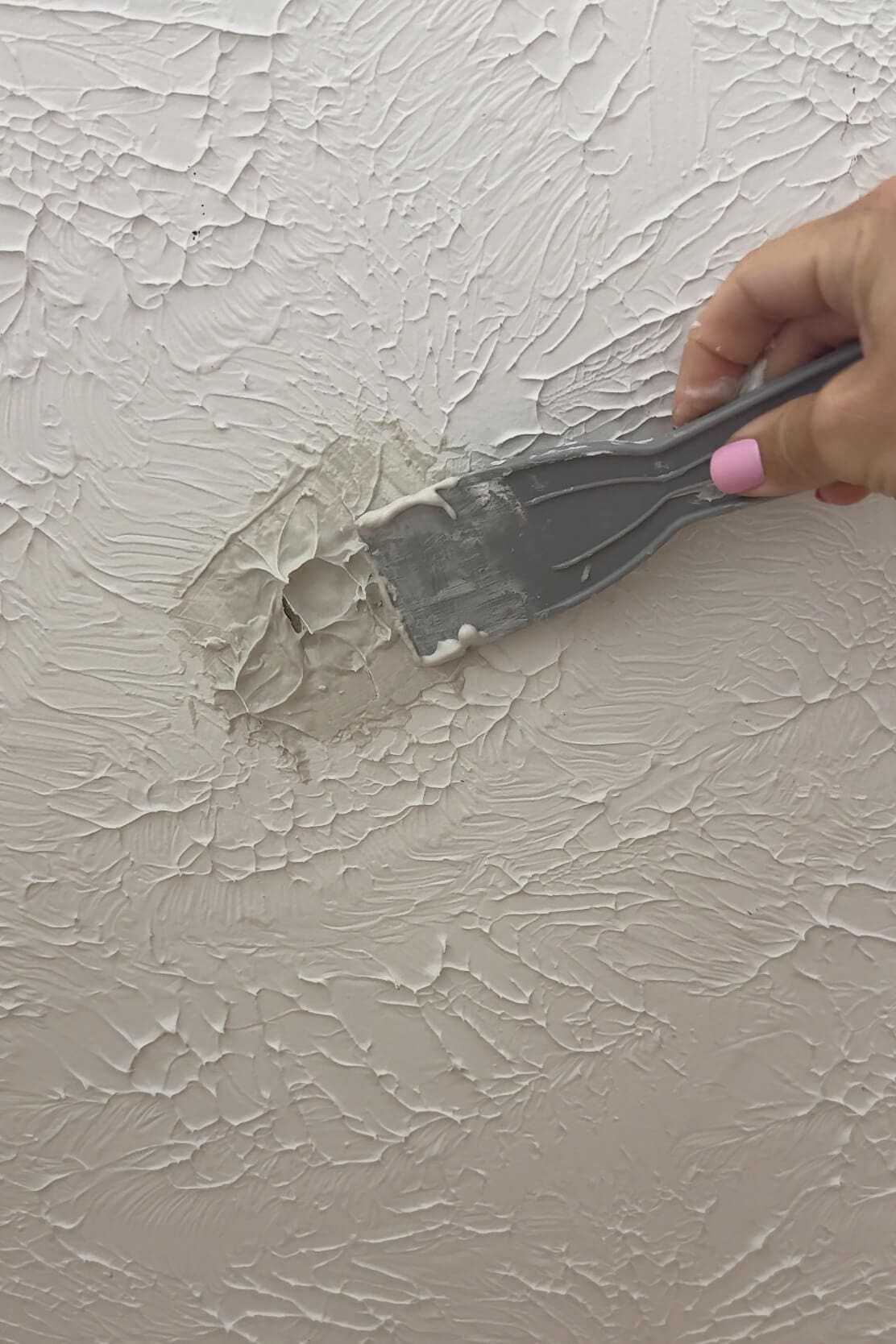 Applying joint compound over a ceiling hole using a putty knife to blend with textured surface