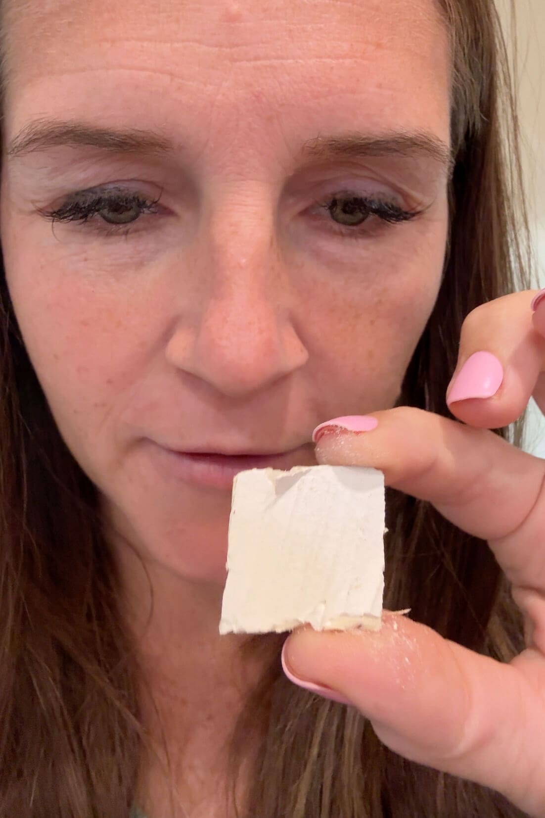 Close-up of a woman holding a small piece of painted drywall to match ceiling paint color