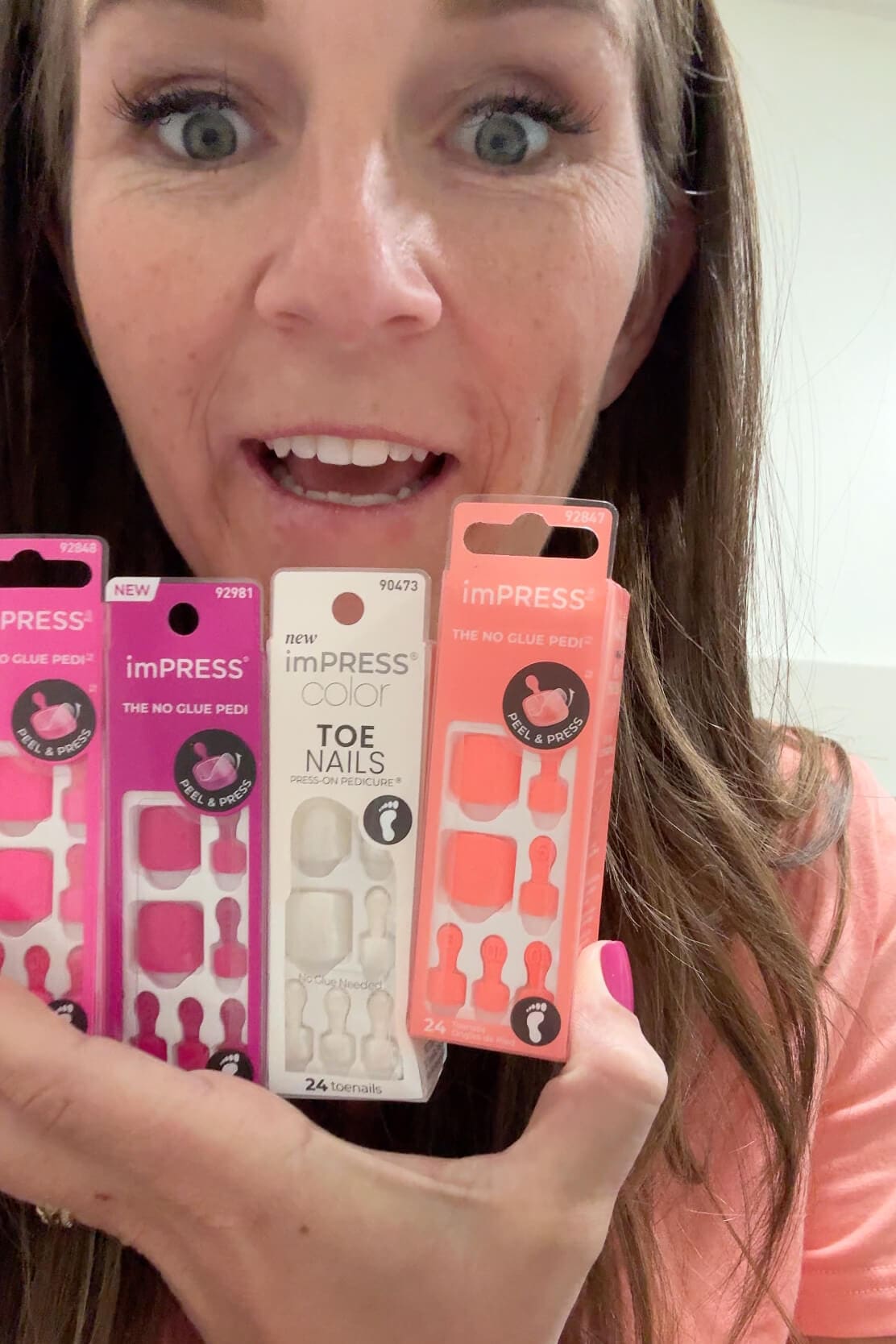 Smiling woman holding up a variety of Kiss Impress Nails packages, including bold colors and pedicure sets.