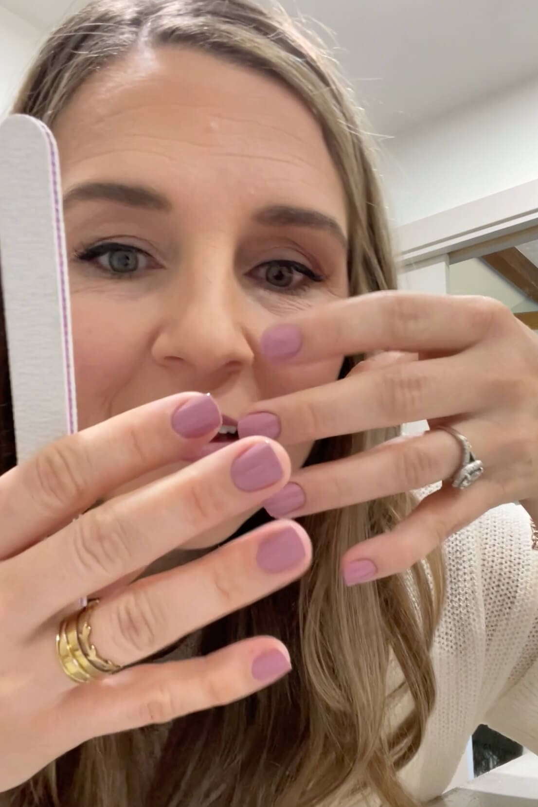 Close-up of hands showing the finished look after applying Kiss Impress Nails in a mauve shade, holding a nail file.