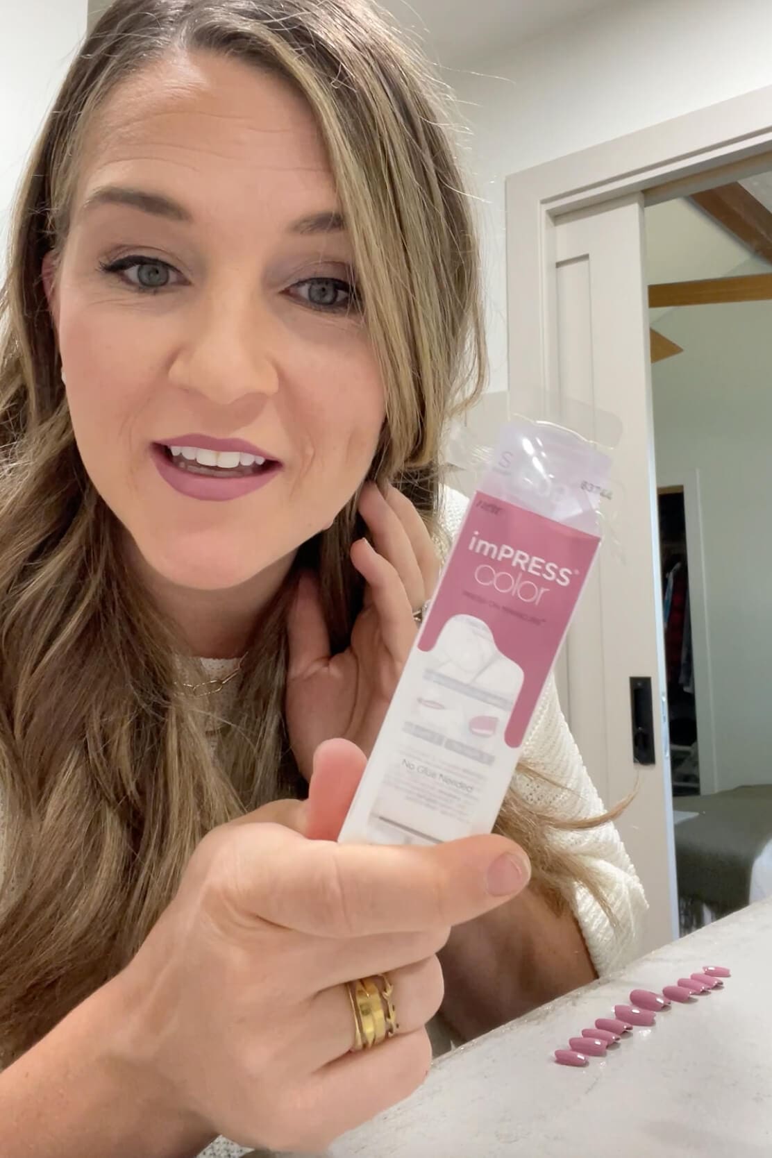 Holding a package of Kiss Impress Nails with a full set laid out on the counter, ready for a step-by-step press-on manicure tutorial.