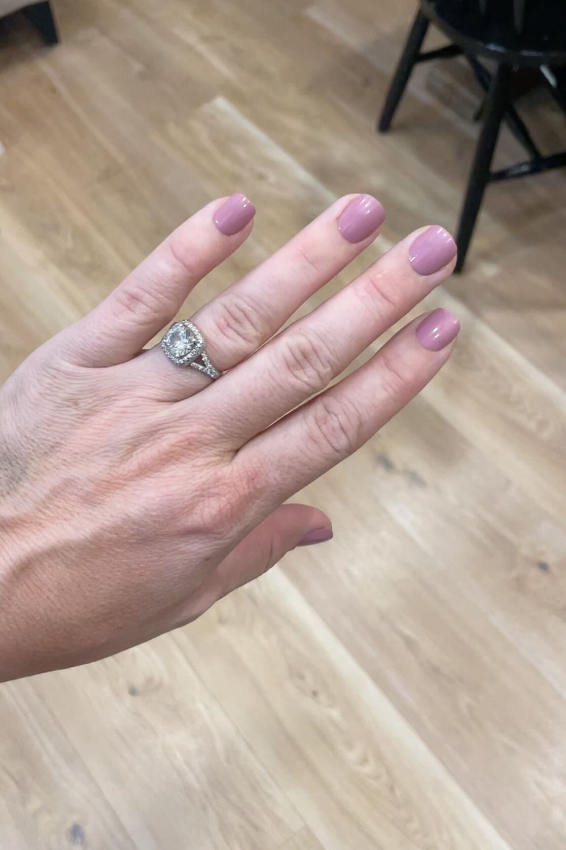 Hand wearing Kiss Impress nails in a soft mauve shade called petal pink, photographed against light wood flooring for a natural at-home manicure look.