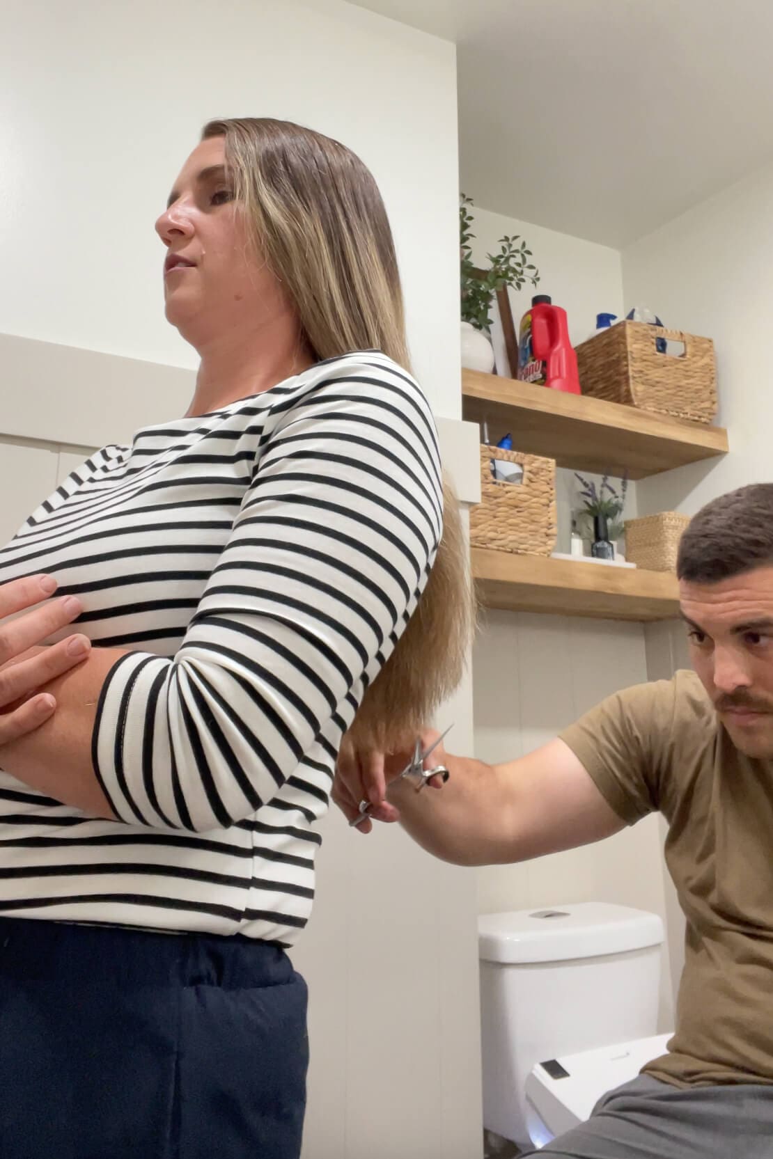 At-home haircut in progress with partner trimming the length of long straight hair.