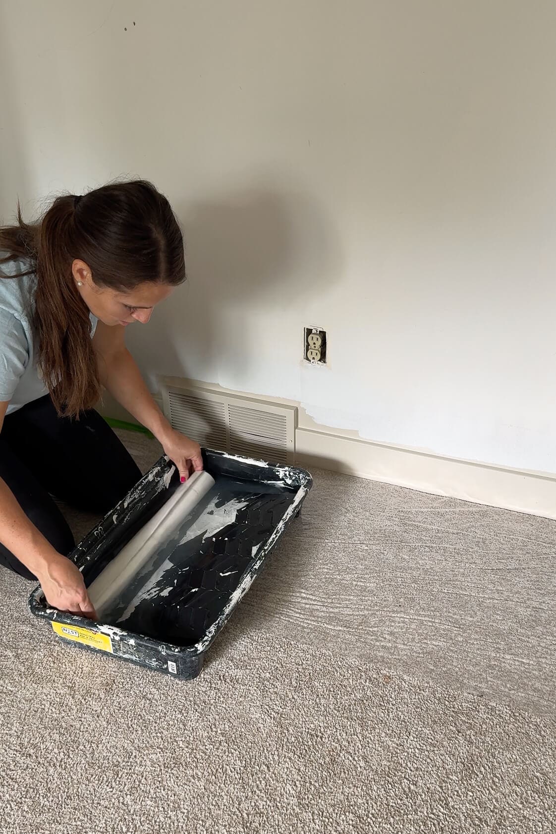 Woman activating the adhesive by rolling it into a tray of water on the floor, next to a primed wall and outlet.