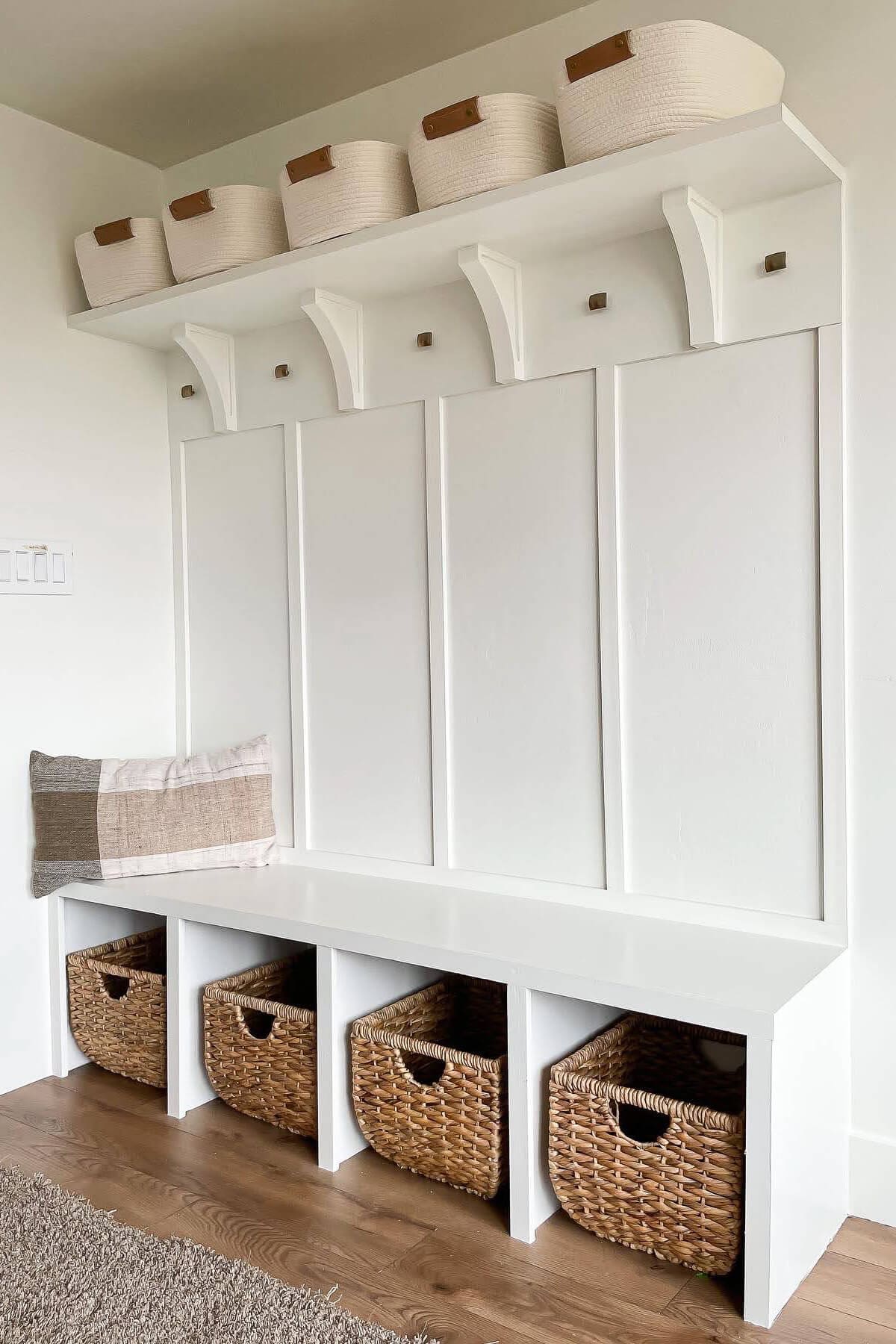 Custom mudroom built-in with white board and batten backing, open cubbies with wicker baskets, wall hooks, and decorative storage bins above.
